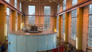 A generator within an old, high-ceiling room surrounded by windows